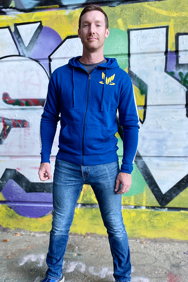 Image shows Mass Effect Team Alenko Hoodie worn by male model facing front. Kaidan was born in 2151 into a family already familiar with space: his father served in the Alliance military. After his mother was downwind of a transport crash in Singapore, Kaidan was exposed in utero to element zero and beat the odds, gaining biotic potential instead of terminal brain cancer.