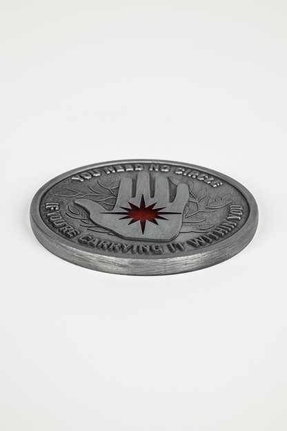 Image shows the Mage Coin laid flat upside down. Mage coin's side B features an embossed pattern of the Arcane Defender emblem with red enamel filling and text that reads, YOU NEED NO CIRCLE IF YOU'RE CARRYING IT WITHIN YOU.