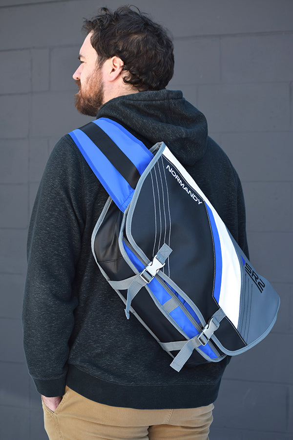 Image shows male facing backwards at an angle weaing the Mass Effect SR2 Alliance Messenger Bag.  The product is comfortable and easy to use with its interior padded securable pocket that fits up to a 17 in laptop.