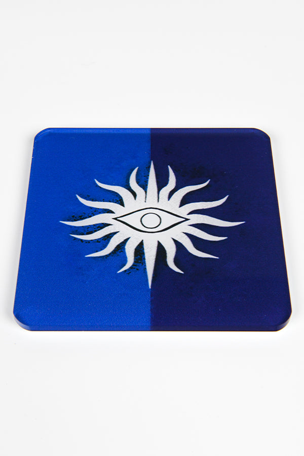 Image shows the Seekers of Truth heraldry symbol.   The symbol is white showing the All Seeing Eye Insignia over a light blue background on the left and dark blue background on the right. 
