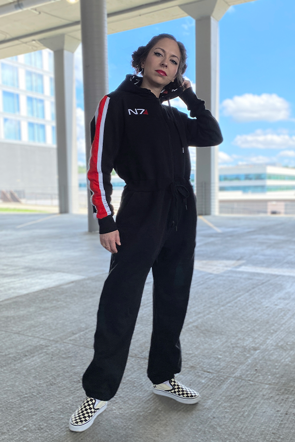 Image shows Mass Effect N7 Adult Onesie Reimagined worn by a female model facing front. Several N7-branded weapons developed by the Systems Alliance see widespread use by 2186. Some of these weapons - along with the capability to manufacture more - are even brought along by the Andromeda Initiative to their new home in the eponymous galaxy.