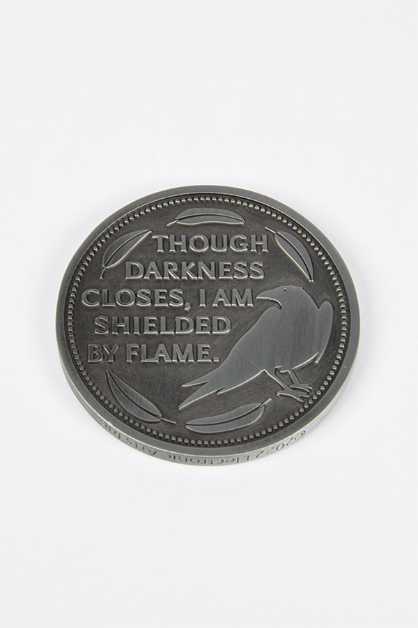 Image shows Dragon Agree Advisors Coin Set with one coin laid flat facing back with the text that reads "Though darkness closes, I am shielded by flame."