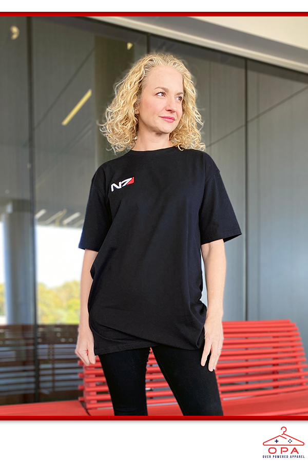 Image shows Mass Effect N7 3D Embroidered OPA T-Shirt worn by female model facing front at an angle. According to The Art of Mass Effect, the red detail on the emblem symbolizes the human blood Shepard must sacrifice to stop Saren Arterius. The red stripe is also a historical reference to the red stripes commanders wore on early space missions to make them instantly recognizable.