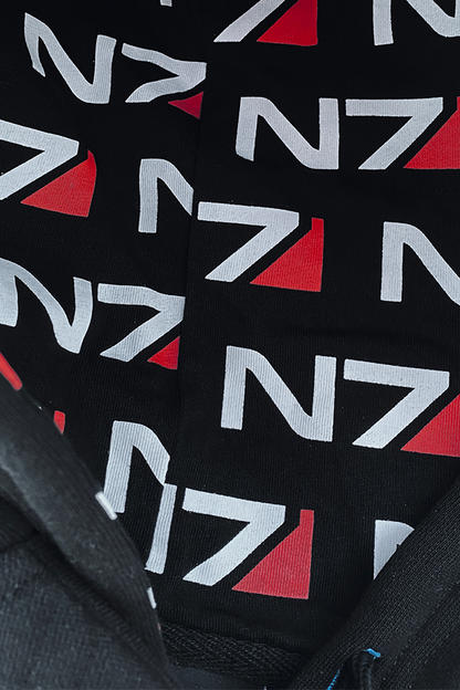 Image shows Mass Effect N7 Adult Onesie Reimagined with the inside of the hoodie zoomed in. According to The Art of Mass Effect, the red detail on the emblem symbolizes the human blood Shepard must sacrifice to stop Saren Arterius. The red stripe is also a historical reference to the red stripes commanders wore on early space missions to make them instantly recognizable.