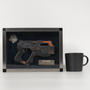 Image shows Mass Effect Carnifex Replica Shadowbox facing front beside a black mug for scale. The gun has a dial on the side with 