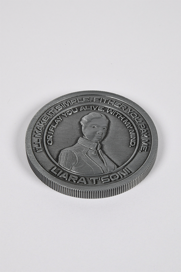Image shows Mass Effect Coin Album's Liara coin laid flat facing front. Coin features Liara's logo in the middle surrounded by one of here famous quotes. Dr. Liara T'Soni is an asari researcher who has spent the past fifty years of her life studying Prothean technology and culture, specialising in the Prothean extinction. She was born on Thessia in 2077, making her "only" 106—barely an adult in asari terms.
