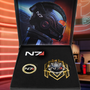 Image shows Mass Effect N7 Premium Box laid flat with th box open. The beautiful case with Mass Effect branding and N7 stripes features a graphic print of Commander Shepard’s helmet and a thick foam insert with a medal, an N7 card, and a Systems Alliance coin.