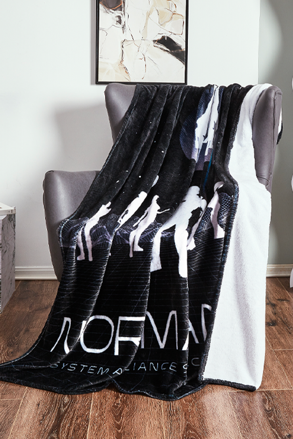 Image shows Mass Effect Team Throw Blanket thrown on top of a chair. Product is a 54 x 70 blanket made with 100% polyester printed flannel fleece with a solid white backside.  