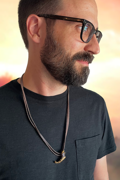 Image shows Dragon Age Solas Jawbone Necklace Jewelry facing front worn by male model. Product features a molded jawbone pendant made with zinc alloy with an antique brass finish.