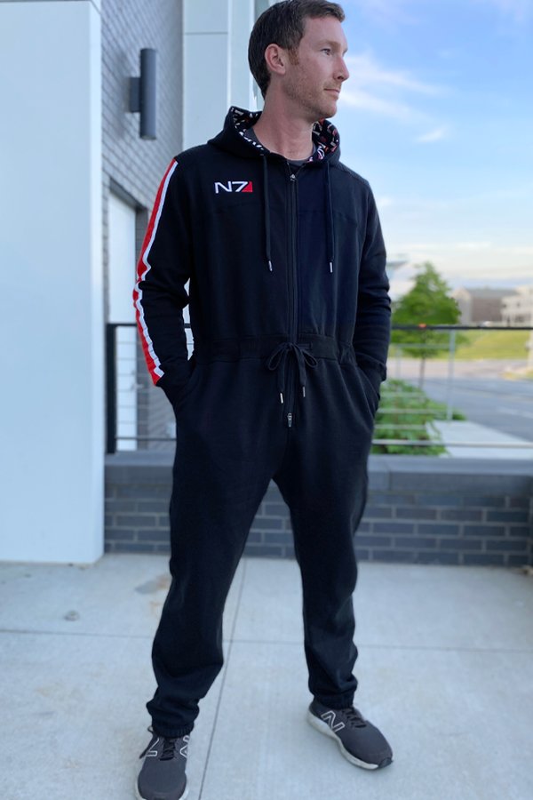 Image shows Mass Effect N7 Adult Onesie Reimagined worn by male model facing front at an angle. Product is black and made with 80% cotton / 20% polyester fleece.