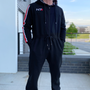 Image shows Mass Effect N7 Adult Onesie Reimagined worn by male model facing front at an angle. Product is black and made with 80% cotton / 20% polyester fleece.