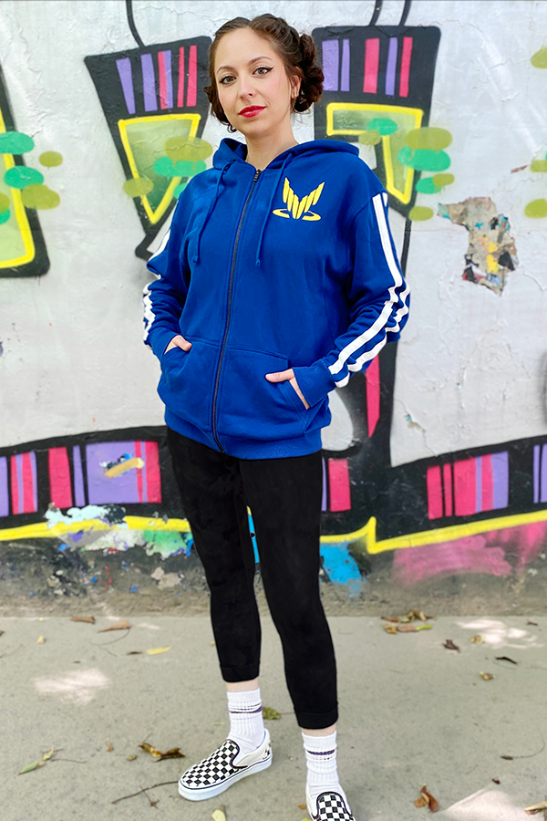 Image shows Mass Effect Team Alenko Hoodie worn by female model facing front. The hoodie features a yellow spectre logo on the wearer's left chest. The hoodie also features white sleeve stripes.