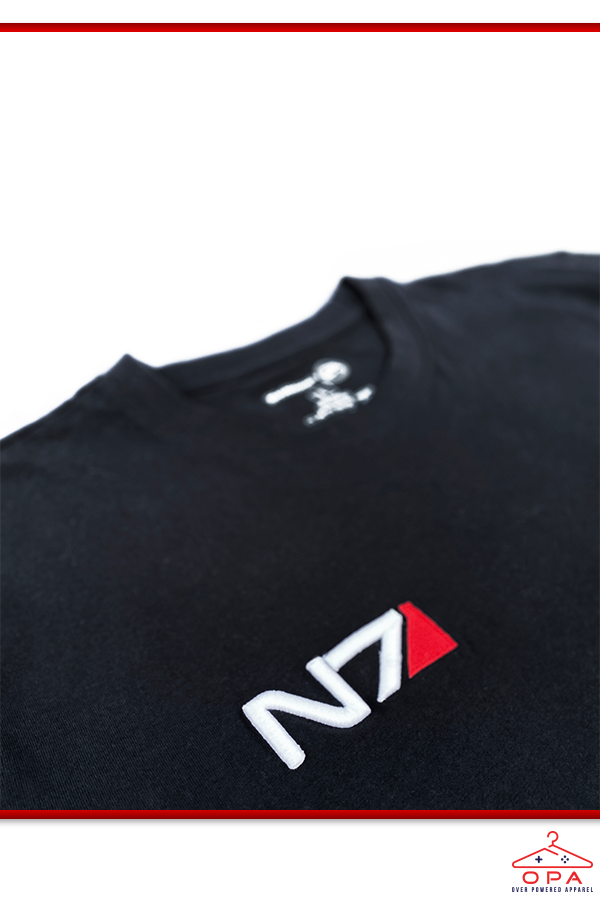 Image shows Mass Effect N7 3D Embroidered OPA T-Shirt laid flat with the upper torso zoomed in. N7 is a vocational code in the Systems Alliance military. The "N" designates special forces and the "7" refers to the highest level of proficiency. It applies to Alliance personnel who have graduated from the Interplanetary Combatives Training (ICT) program.