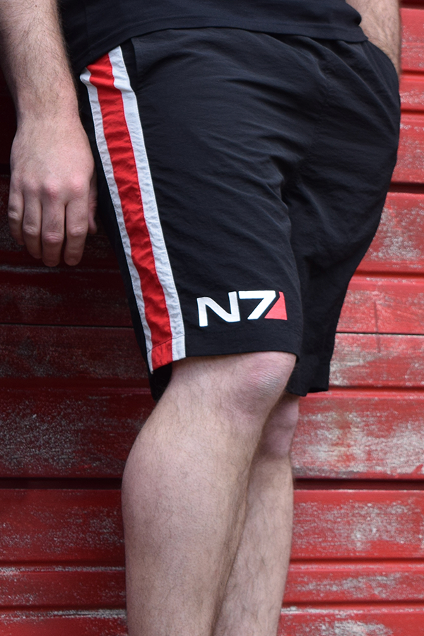 Image shows Mass Effect N7 Active Shorts worn facing at an angle. Product is made with 100% Nylon Twill and features an elastic waistband with drawcord. 