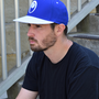 Image shows Mass Effect Blue Suns Hat worn by male model facing at an angle. Product is a classic unisex hat and a great addition to sports jackets and hoodies.