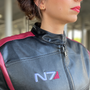 Image shows Mass Effect N7 Jacket Reimagined worn by female model facing at an angle. Jacket features a left chest interior zip pocket.