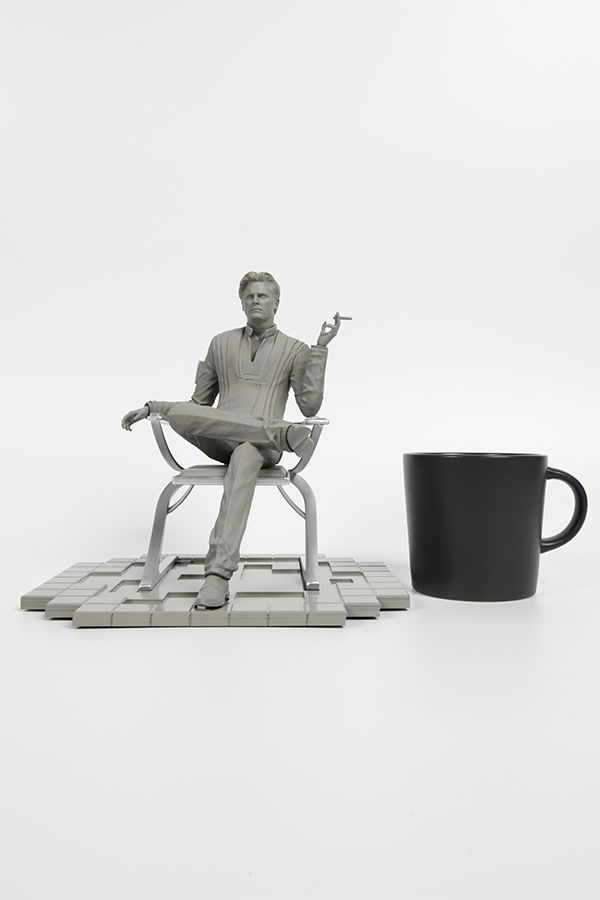 Image shows Illusive Man Prototype Statue beside a black coffee mug. Product is 22cm in length, 20cm in width and 21.8cm in height. 