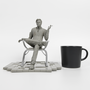 Image shows Illusive Man Prototype Statue beside a black coffee mug. Product is 22cm in length, 20cm in width and 21.8cm in height. 