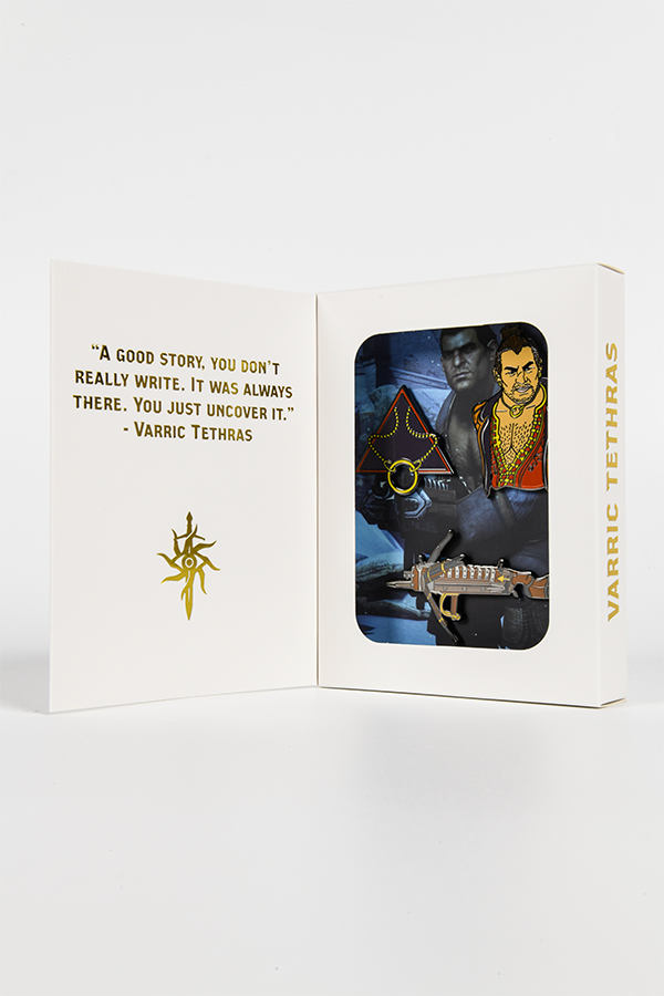 Image shows Dragon Age Varric Pin Set inside its box with the box standing upright wide open. 