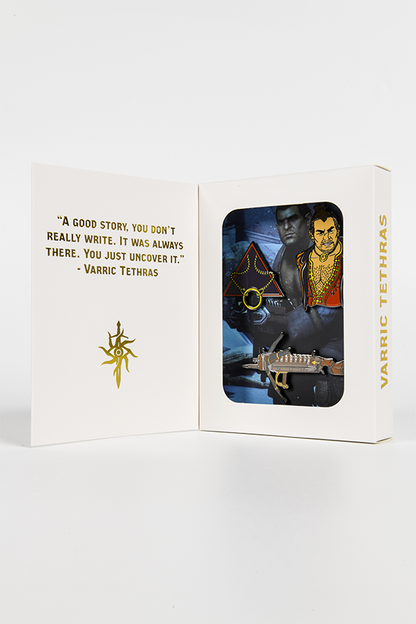 Image shows Dragon Age Varric Pin Set inside its box with the box standing upright wide open. 