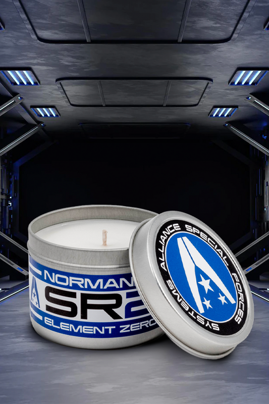 Image shows Mass Effect Element Zero Scented Candle facing front with its cap opened leaning on its side. This scented candle comes in a 6oz tin and is made using coconut soy wax. With a burn time of 40 hours, the Mass Effect Element Zero Scented Candle permeates its rich orange and cedar wood fragrance throughout your home. The tin features SSV Normandy labels, making it look like an eezo storage container.